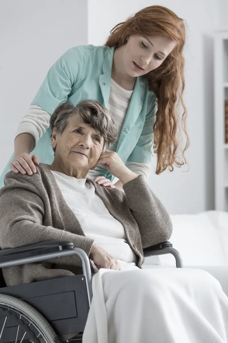 A caregiver gently comforting an older woman in a wheelchair