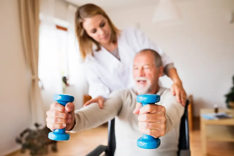 Cúramóir ag cabhrú le fear aosta le haclaíocht éadrom sa bhaile