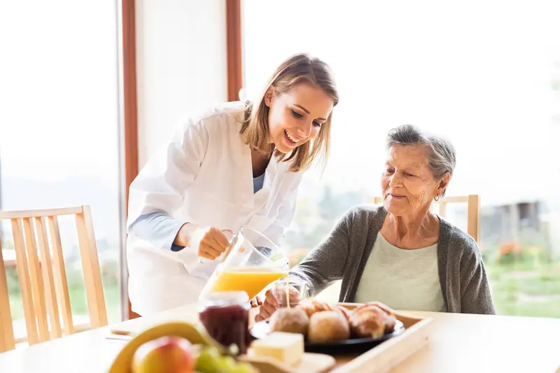 A caregiver serving a healthy meal to a smiling older woman