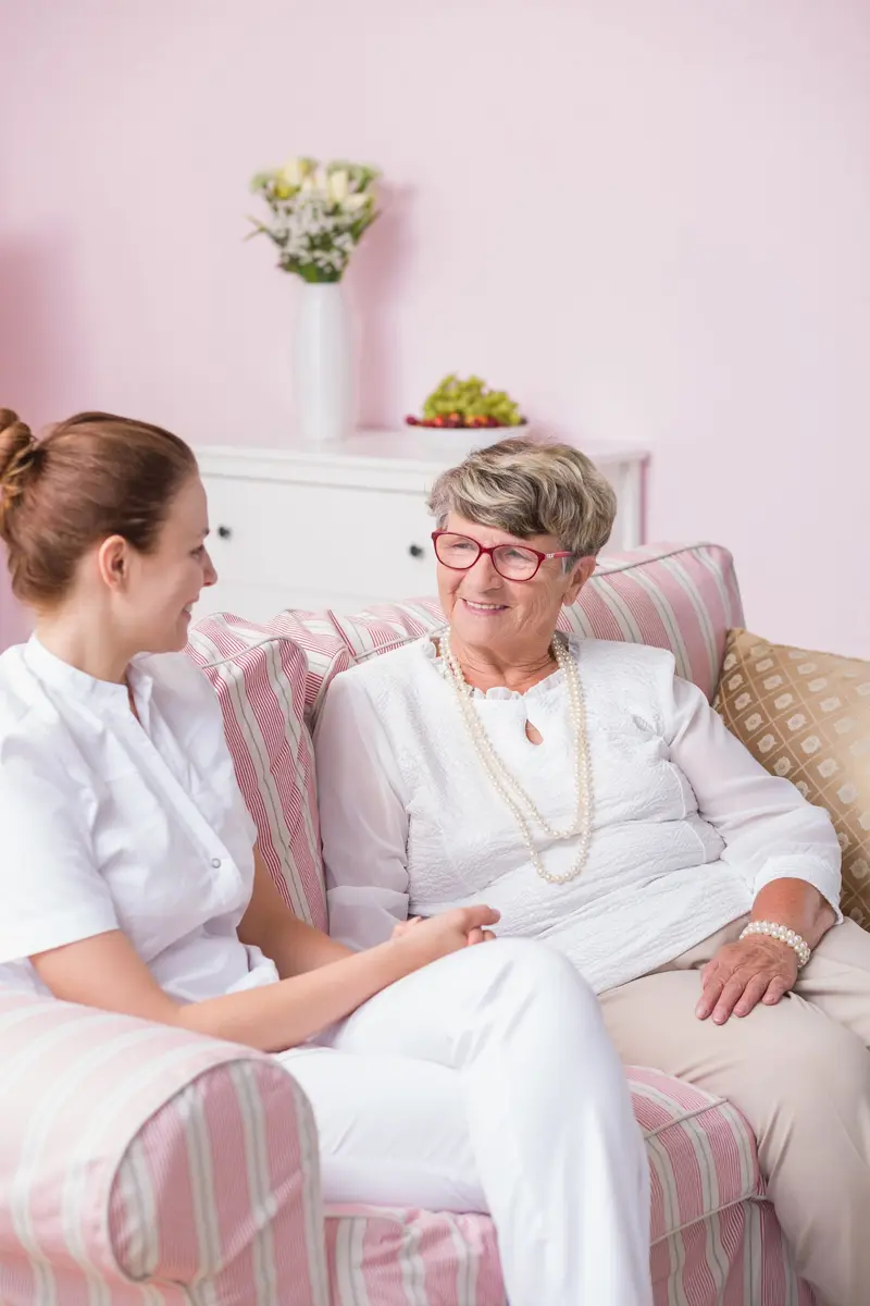 A caregiver sitting with a smiling older woman on a sofa